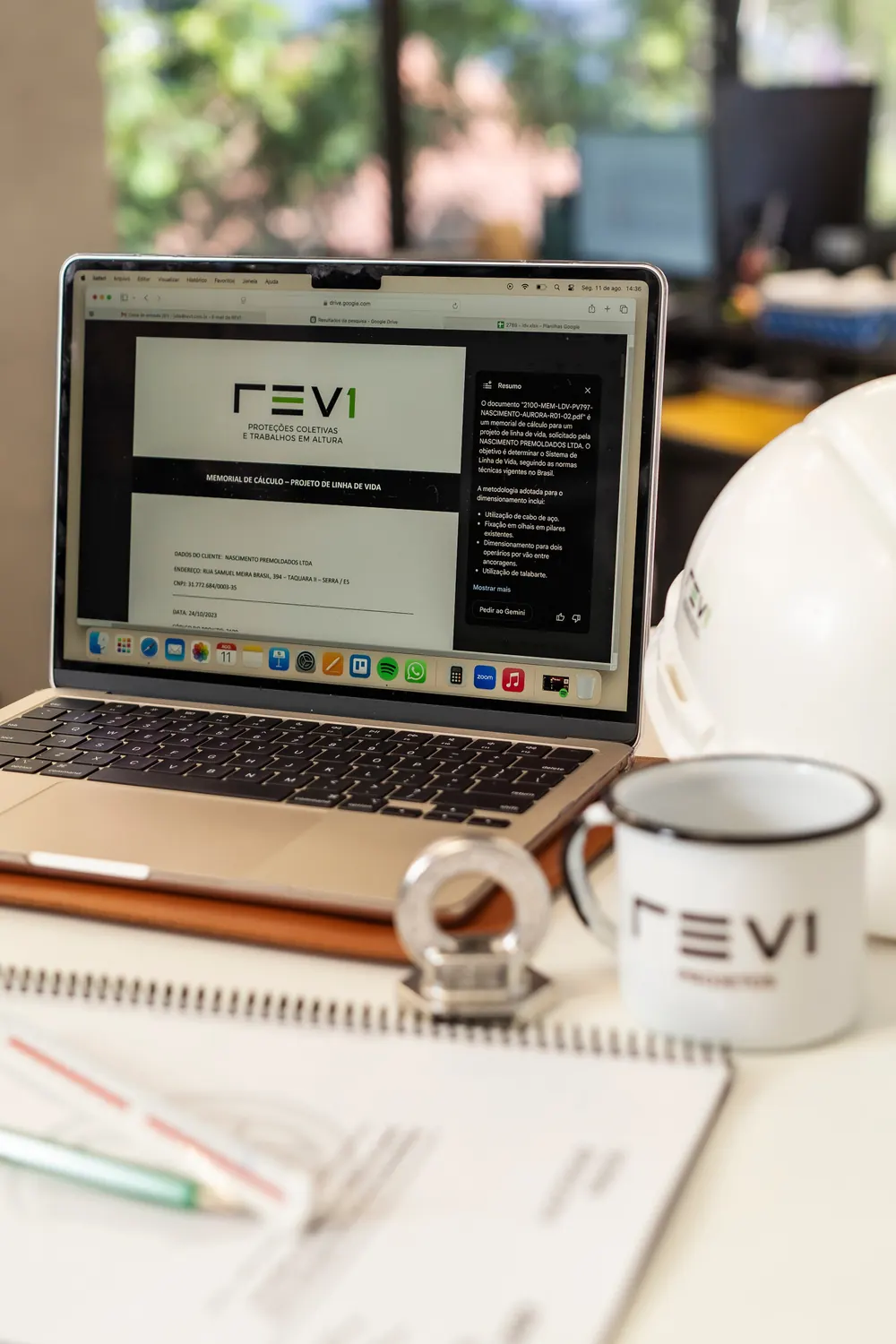 Notebook com projeto REV1 aberto, capacete e caneca sobre a mesa